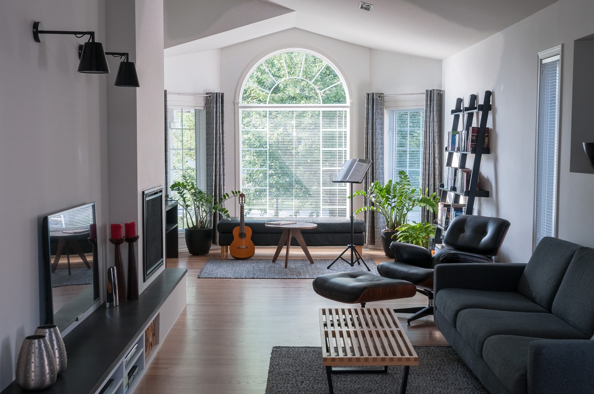 Bright living room with an arched window, a dark leather sofa and a lounge chair
